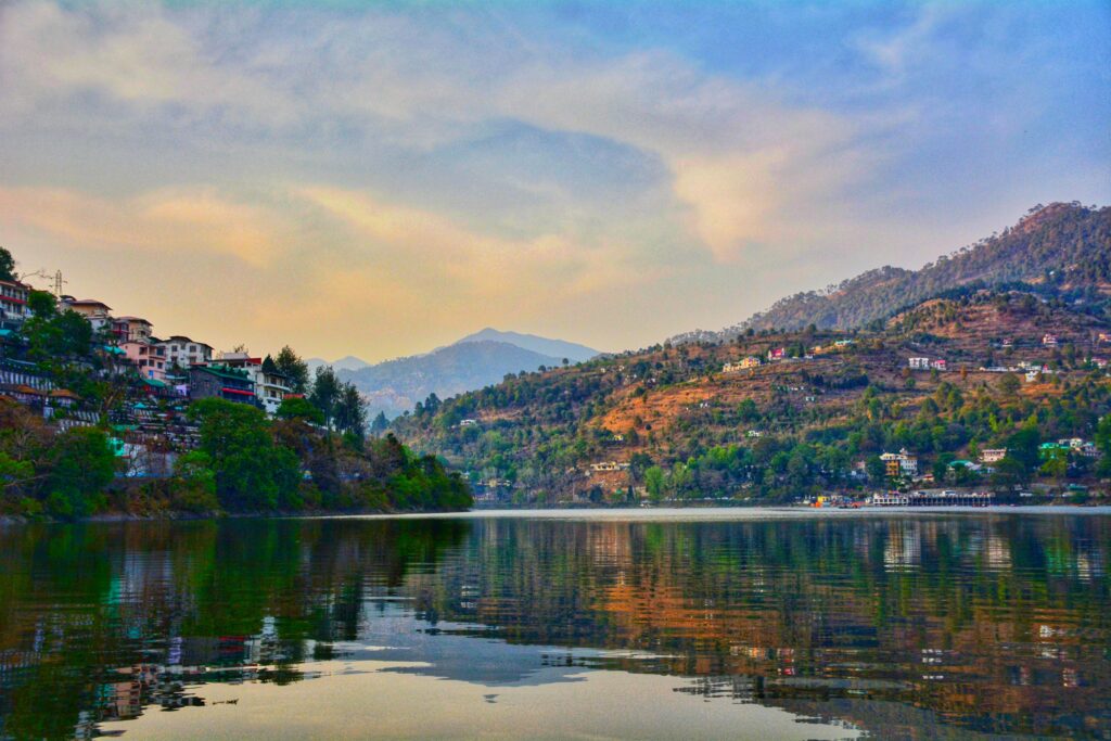 A picturesque view of Bhimtal Lake with hills, houses, and serene sky reflection, Uttarakhand, India.
